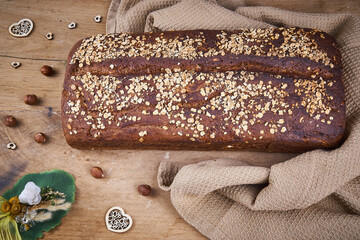 Schwarzbrot mit Haseln&uuml;ssen ungeschnitten mit Handtuch auf Holzbrett