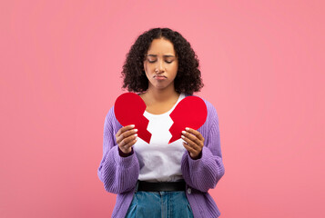 Unhappy millennial black woman holding halves of broken heart, having relationship problems over...