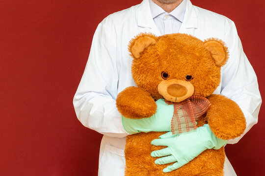 Doctor with teddy bear.Cropped image of male pediatrician holding little teddy bear.Healthcare and medicine.Red studio background.copy space.