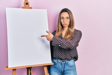 Beautiful hispanic woman pointing to painter easel stand depressed and worry for distress, crying angry and afraid. sad expression.