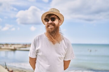 Young redhead tourist man smiling happy standing at the beach.