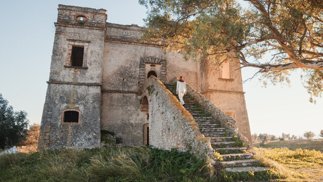 Beautiful girl in white dress enters an ancient castle in the countryside 
