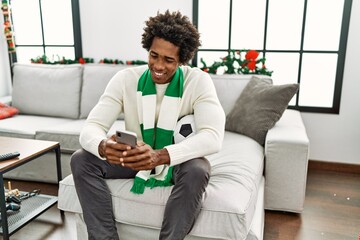 Young african american hooligan man using smartphone supporting soccer team sitting on the sofa at...