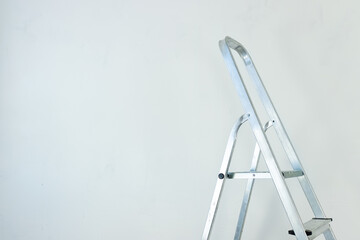Folding aluminum staircase in an empty room on a white wall background.