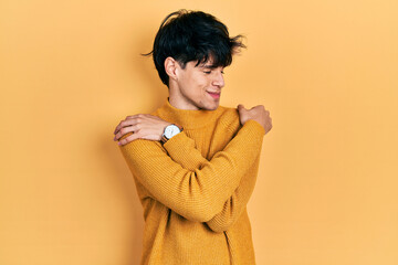 Handsome hipster young man wearing casual yellow sweater hugging oneself happy and positive, smiling confident. self love and self care