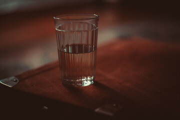 Keeping healthy and staying hydrated with a glass of iced water at home or restaurant on blurred background of green dining table and wooden chair.