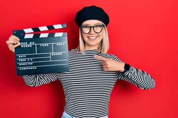 Beautiful blonde woman holding video film clapboard smiling happy pointing with hand and finger