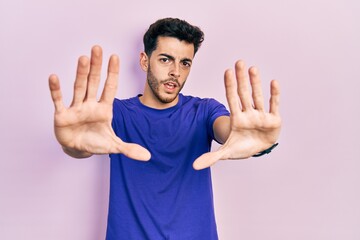 Young hispanic man wearing casual t shirt doing stop gesture with hands palms, angry and frustration expression