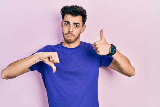 Young hispanic man wearing casual t shirt doing thumbs up and down, disagreement and agreement expression. crazy conflict