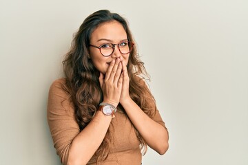 Young hispanic girl wearing casual clothes and glasses laughing and embarrassed giggle covering mouth with hands, gossip and scandal concept - obrazy, fototapety, plakaty