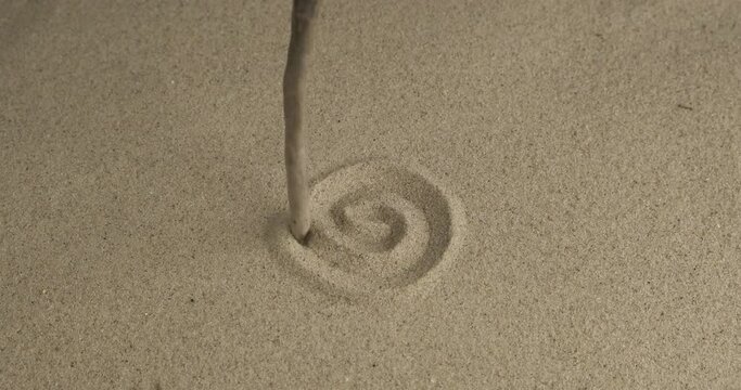 Drawing a spiral on spinning sand with a wooden stick. Beautiful effect