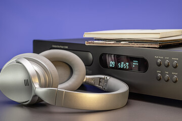 CD player and headphones for listening to music, close-up. Lilac background, CD in envelopes.