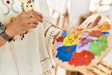 Young hispanic woman mixing color on palette at art studio