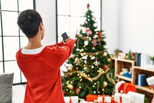 Young hispanic woman make photo by the smartphone to christmas tree at home