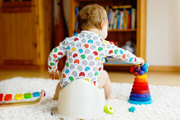 Closeup of cute little 12 months old toddler baby girl child sitting on potty.