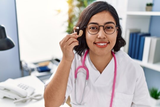 Young latin woman wearing doctor uniform holding hearing aid machine at clinic