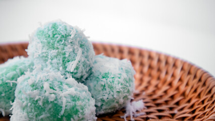 extreme close upklepon or green sticky rice balls filled with liquid palm sugar and coated in grated coconut in a white background