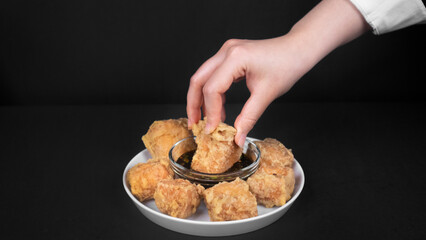 hand dipping one fried tofu fritters to a chilli soybean sauce