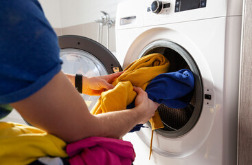 Man loading the washer dryer with clothes - Powered by Adobe