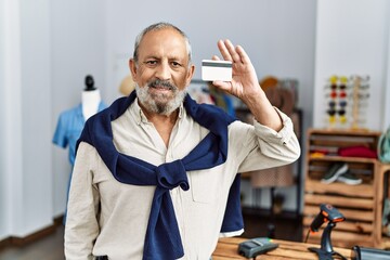 Senior grey-haired man smiling confident holding credit card at clothing store