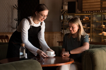 smiling waitress in apron serves coffee to beautiful business blond woman in a cafe. 