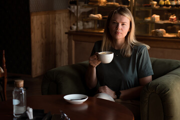 Beautiful blonde woman sits in coffeehouse and bakery and drinks cappuccino coffee
