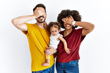 Interracial young family of black mother and hispanic father with daughter smiling and laughing with hand on face covering eyes for surprise. blind concept.