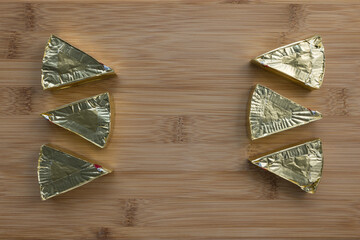 Pieces of processed cream cheese spread on wooden cutting board. Family portion of six triangles in gold foil. Minimalist background. Close-up, top view, copy space
