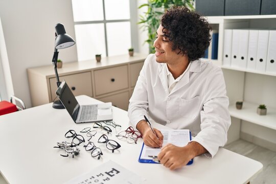 Young hispanic man optician writing on clipboard at clinic