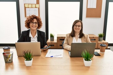 Group of two women working at the office. Mature woman and down syndrome girl working at inclusive...