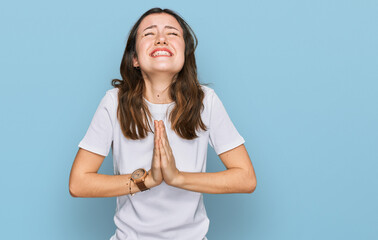 Young beautiful woman wearing casual white t shirt begging and praying with hands together with...