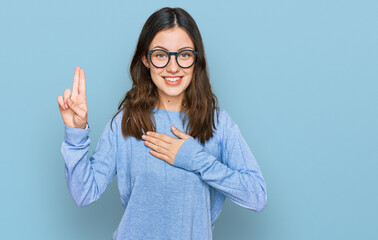 Young beautiful woman wearing casual clothes and glasses smiling swearing with hand on chest and...