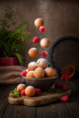 Obraz na płótnie Canvas Homemade Donut Holes sprinkled with sugar with raspberries. Castagnole or Frittelle or Frittole, Italian fried doughnut. Food levitation. Dark background.