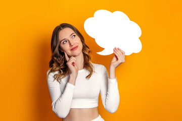 Student girl thought and holding blank speech bubble in the shape of a cloud isolated on an orange background. Copy space