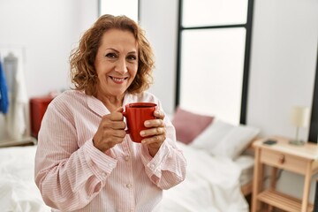 Middle age caucasian woman drinking coffee standing at bedroom.
