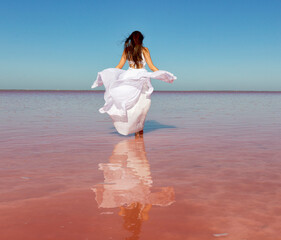 Beautiful woman in a white dress on a pink lake on a summer sunny day