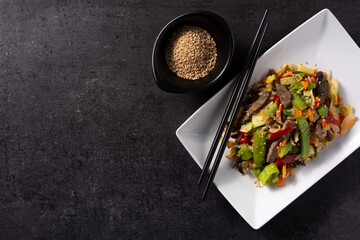 Beef, vegetables and sesame seeds in white plate on black background.Top view. Copy space