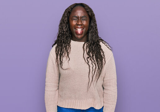 Young african woman wearing wool winter sweater sticking tongue out happy with funny expression. emotion concept.