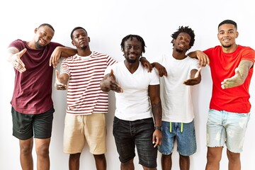 Obraz premium Young african group of friends standing together over isolated background smiling friendly offering handshake as greeting and welcoming. successful business.
