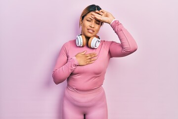 Beautiful hispanic woman wearing gym clothes and using headphones touching forehead for illness and fever, flu and cold, virus sick