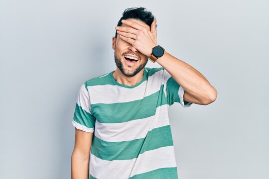 Young hispanic man wearing casual clothes smiling and laughing with hand on face covering eyes for surprise. blind concept.