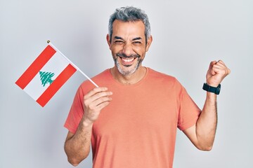 Handsome middle age man with grey hair holding lebanon flag screaming proud, celebrating victory and success very excited with raised arm