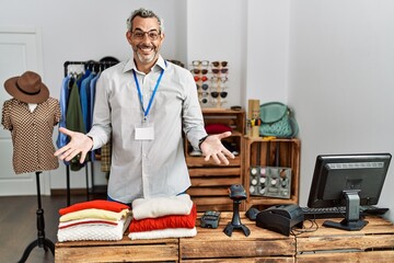 Middle age hispanic man working as manager at retail boutique smiling cheerful with open arms as friendly welcome, positive and confident greetings