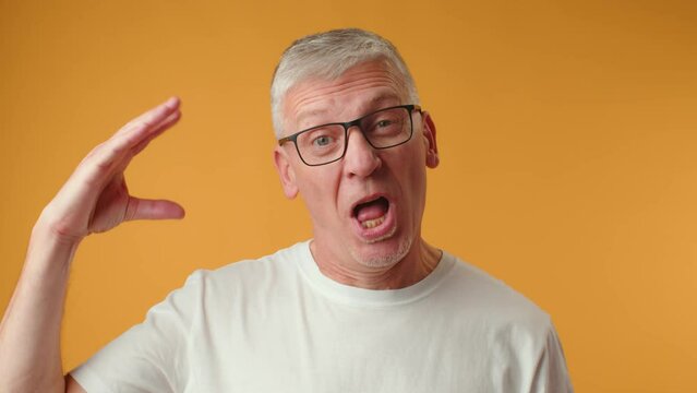 Senior man in glasses doing bla bla gesture against yellow background