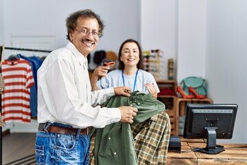 Middle age man and woman smiling confident scanning clothes using bardcode reader at clothing store