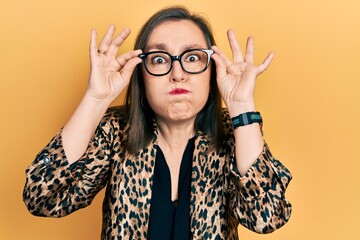 Middle age hispanic woman wearing business clothes and holding glasses puffing cheeks with funny...