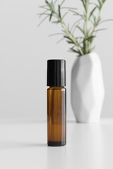 Amber glass roll-on bottle mockup with a rosemary on the white table.
