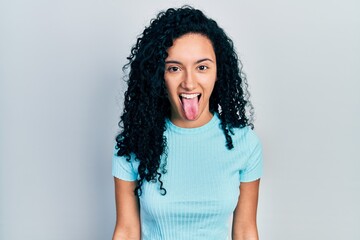 Young hispanic woman with curly hair wearing casual blue t shirt sticking tongue out happy with funny expression. emotion concept. © Krakenimages.com