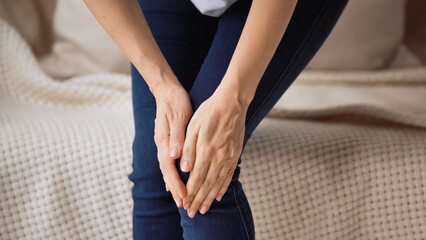 cropped view of woman touching painful knee while standing at home - obrazy, fototapety, plakaty