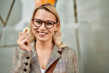 Young blonde businesswoman smiling happy holding bitcoin at the city.